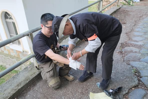 A man bends over to bandage another man's wrist in a civil defense exercise