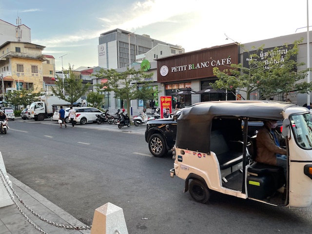 A tuktuk drives down a street, past a cafe