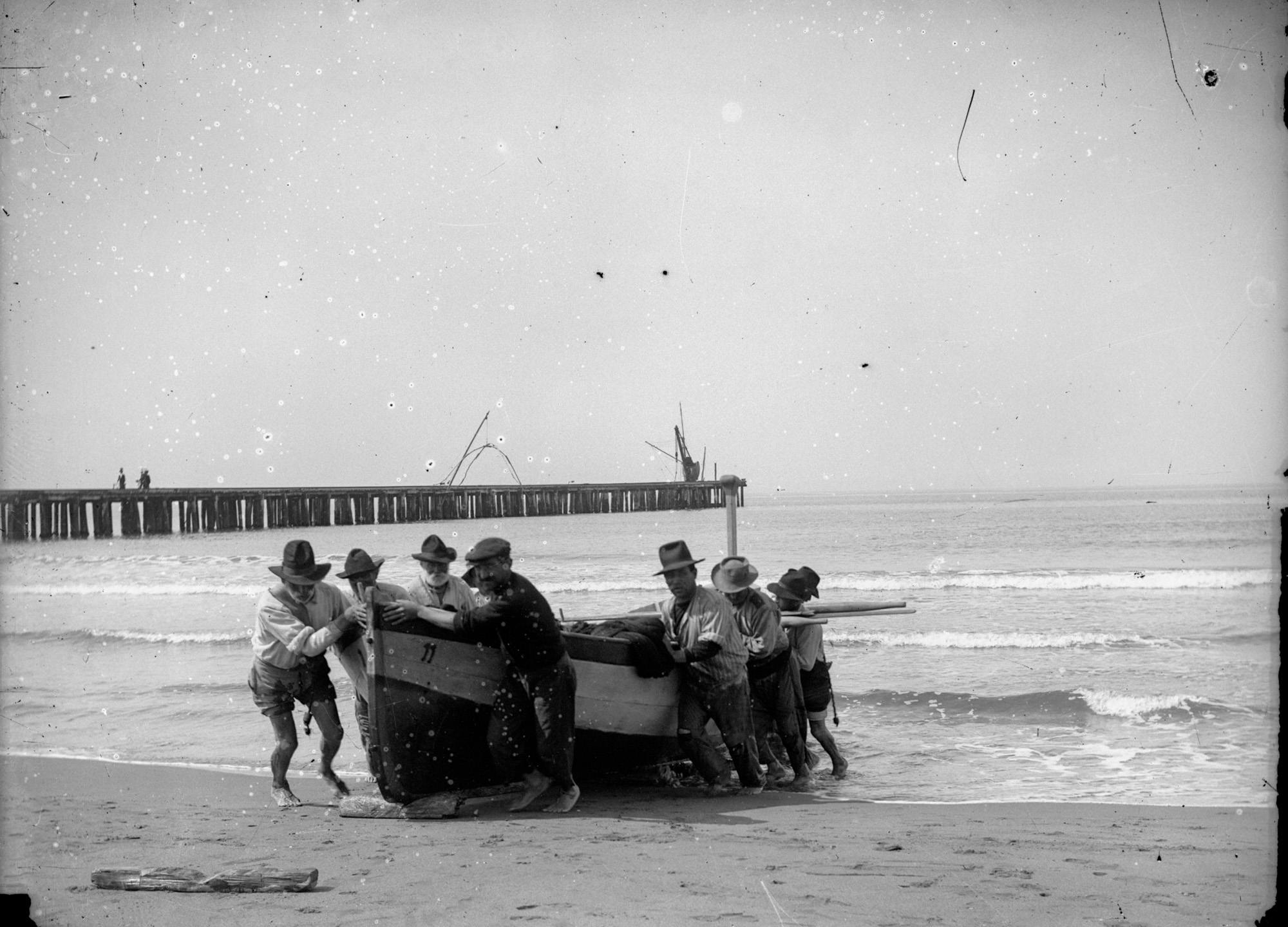 Un'imbarcazione viene messa in secca a forza di braccia dai pescatori sulla spiaggia di Forte dei Marrmi. Primi del Novecento