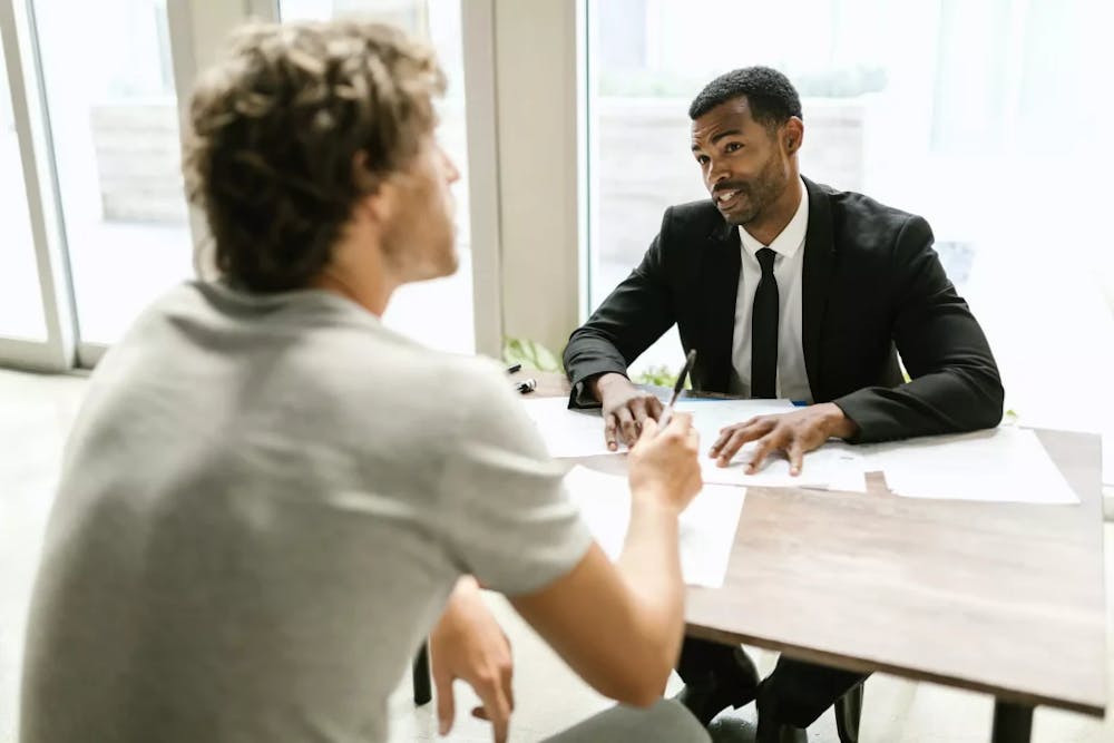 An attorney speaking with their client sitting at a desk.