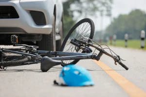 A bike and car in an accident with a helmet in the road.