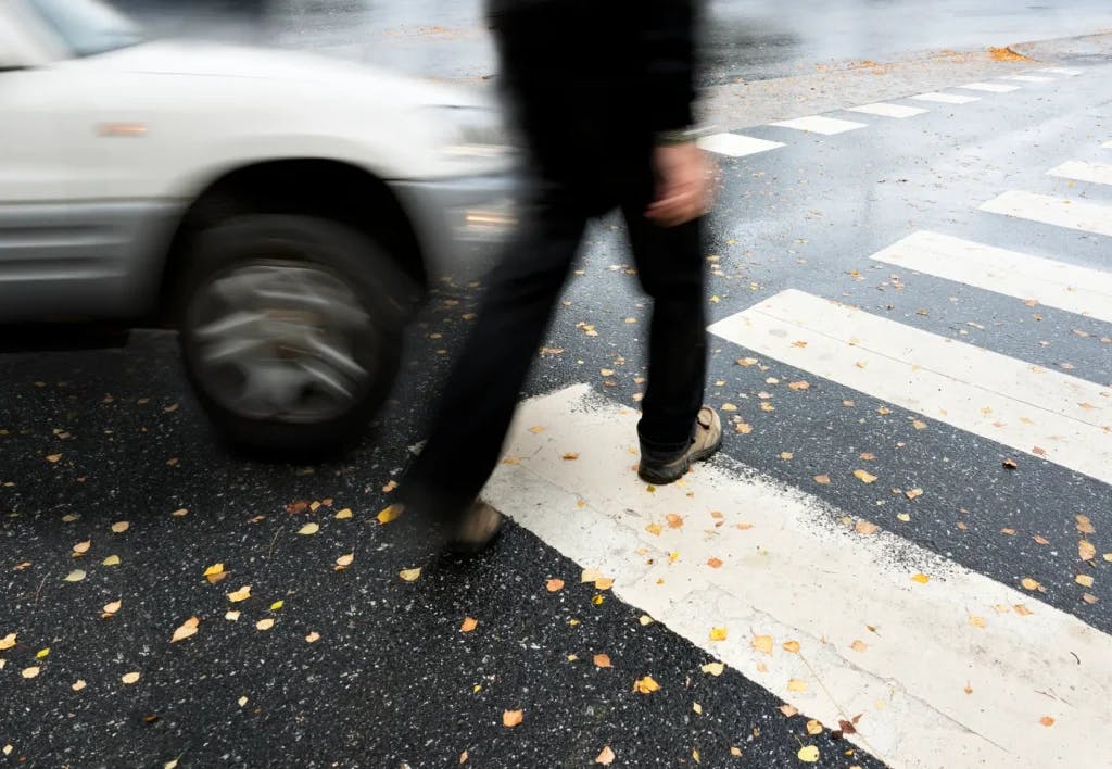 A pedestrian crossing the street about to get hit by a car.