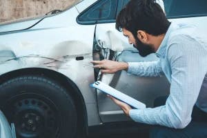 An insurance adjuster assessing a vehicle's damage while the driver compiles their evidence of the accident.;/m,n;/