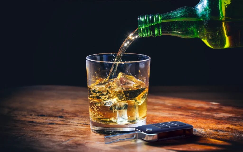 Someone pouring a drink with car keys on the bar.