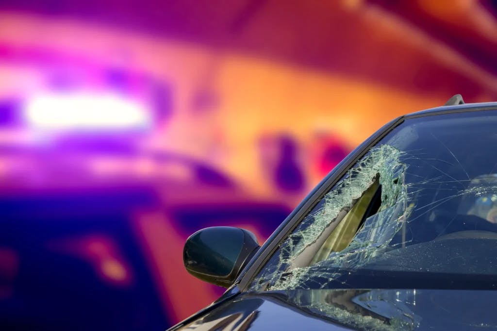 A car that has been in an accident at night with the police car and lights behind it.