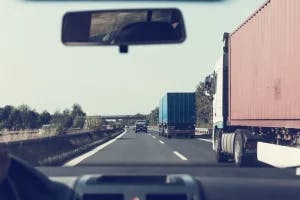 A car driving down the highway surrounded by commercial trucks.