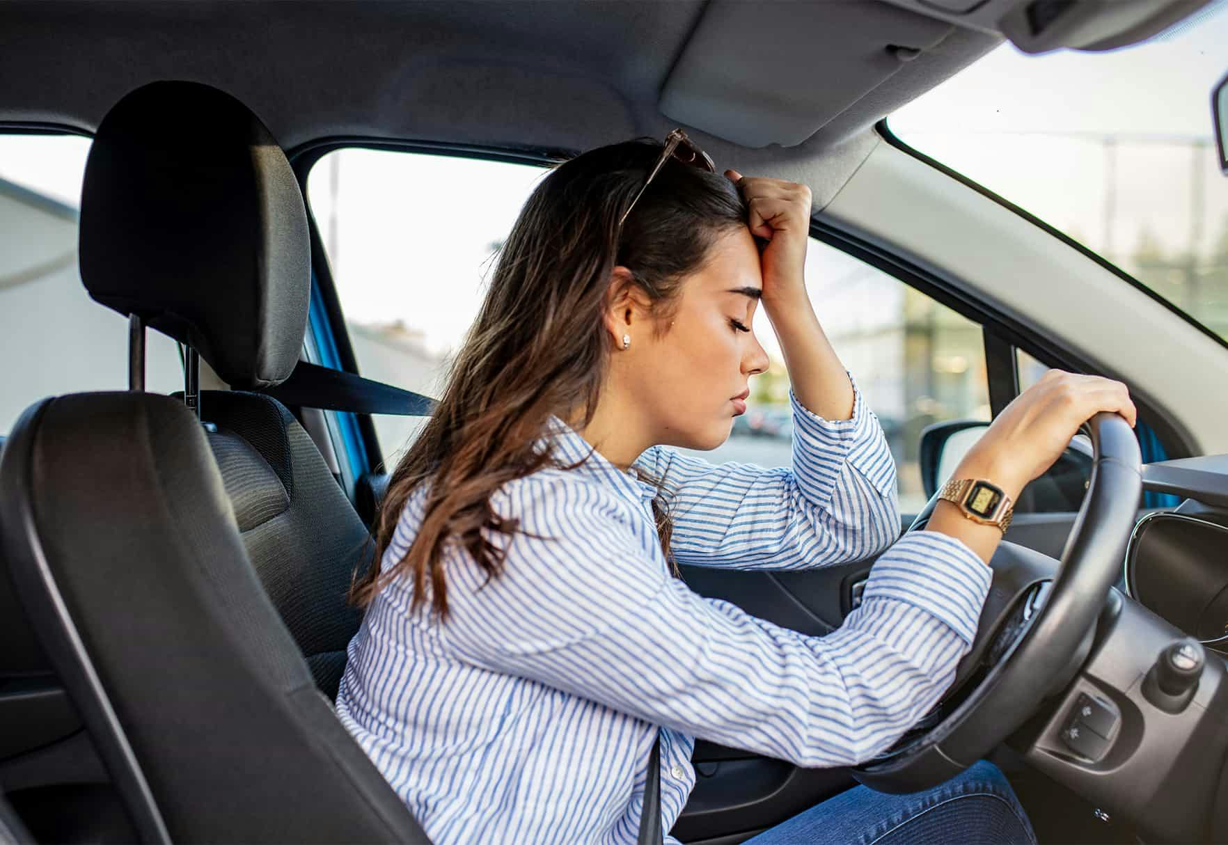 Woman holding head behind the wheel of a car