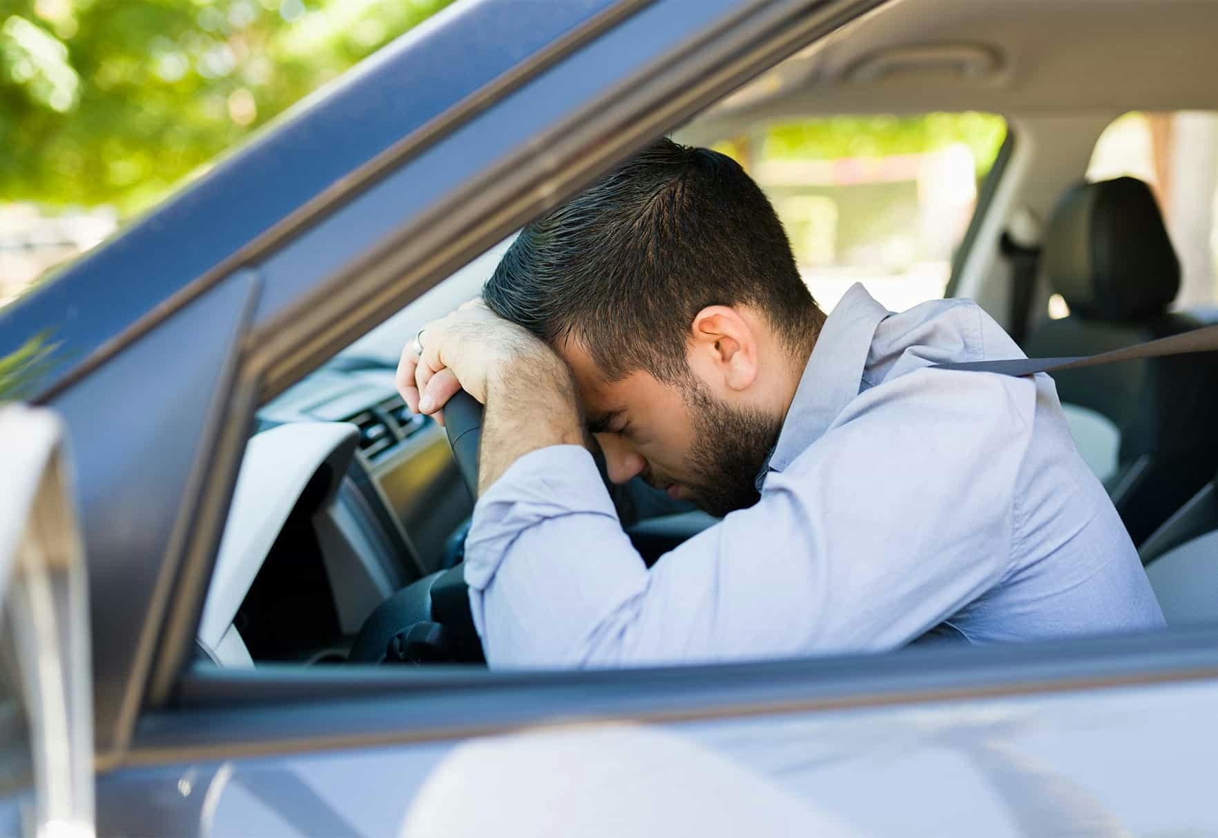 Man with head on car steering wheel