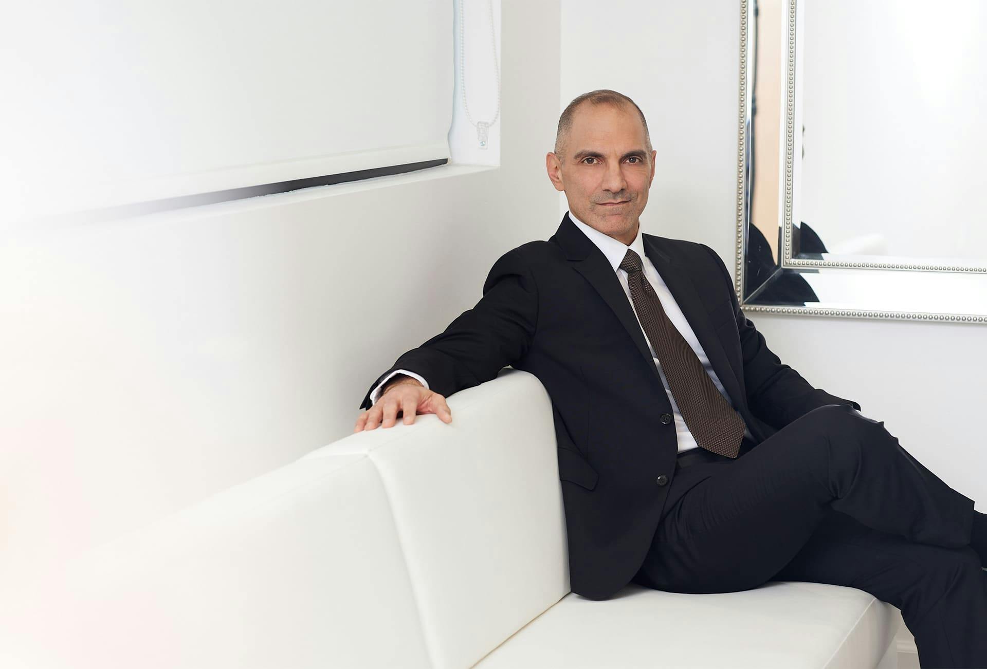 Dr. Panossian in suit sitting on white couch