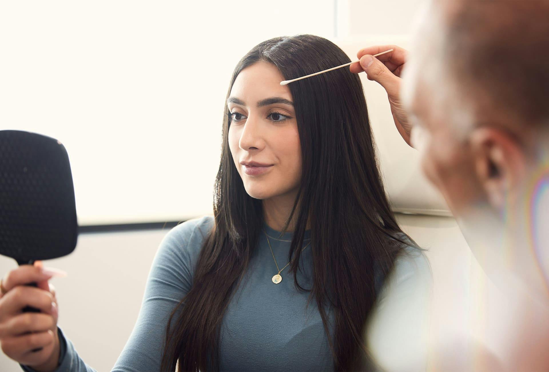 patient holding handheld mirror while Dr. Panossian looks at her eyebrows