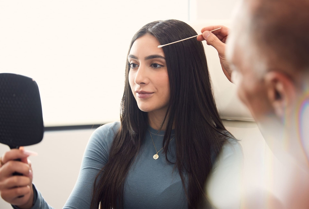 patient holding handheld mirror while Dr. Panossian looks at her eyebrows
