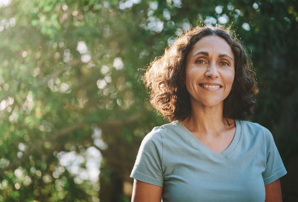 older woman in blue shirt smiling with trees in background