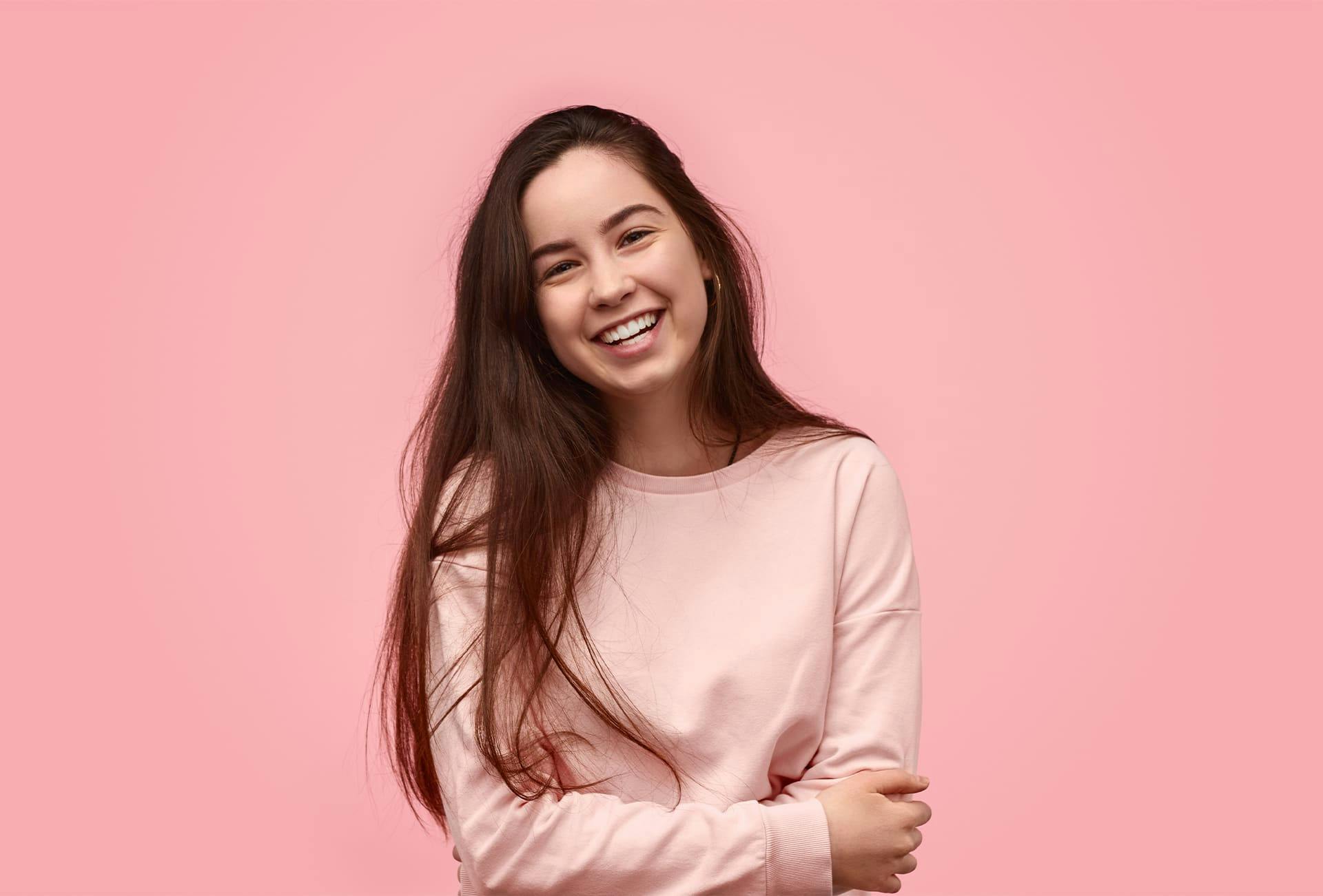 woman smiling with arms crossed with pink background
