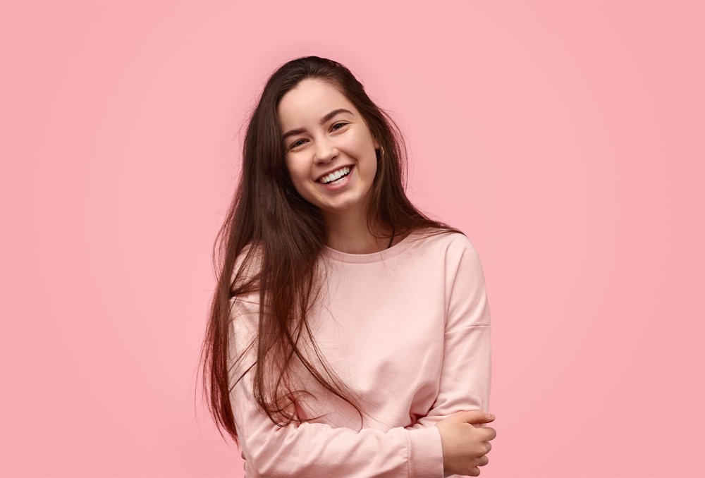 woman smiling with arms crossed with pink background