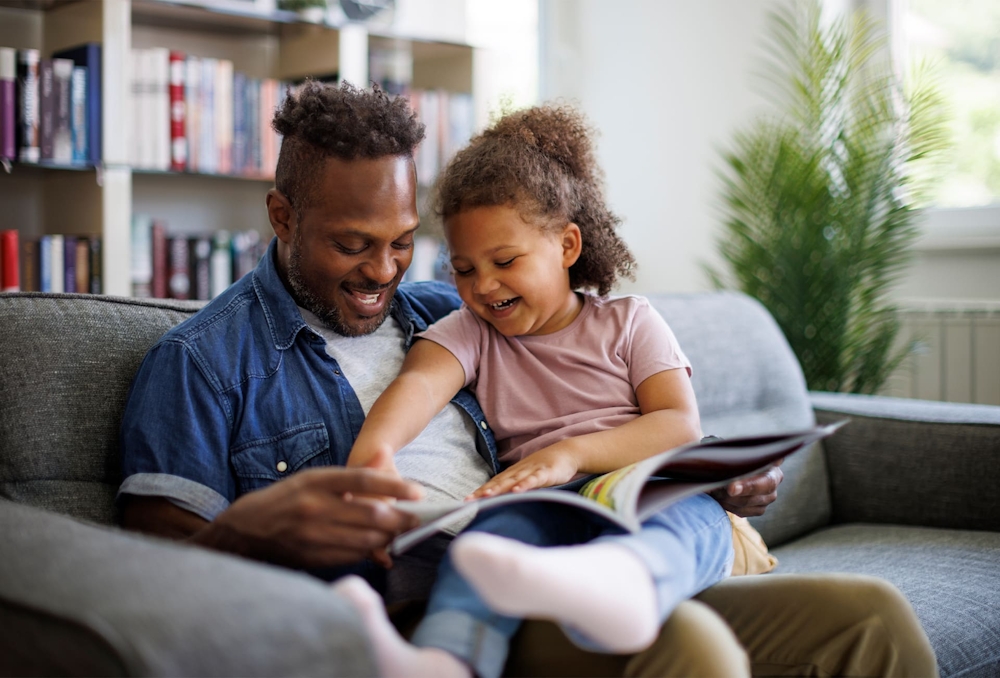 father and daughter reading a kid's book together on couch