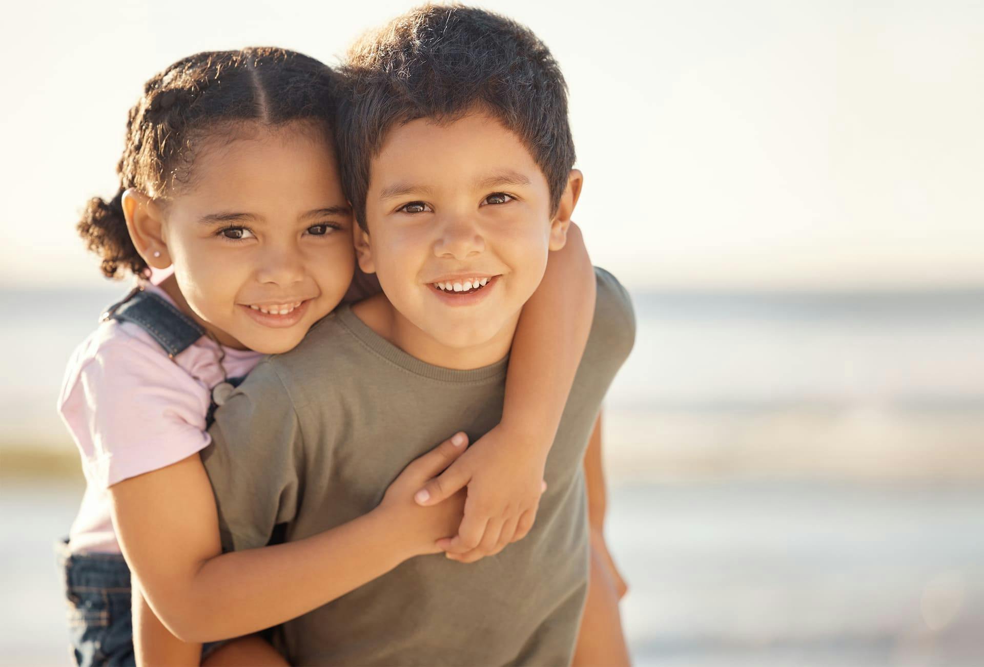 2 kids smiling while giving a piggy-back ride to the other