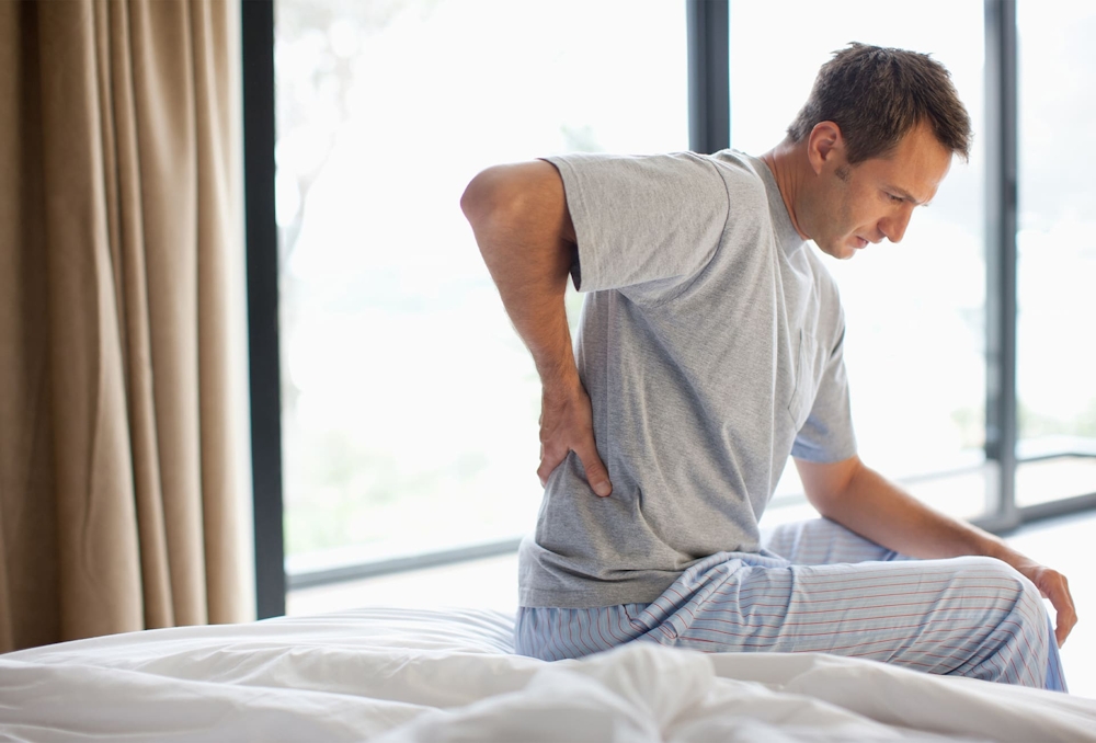 man touching his back while sitting in bed