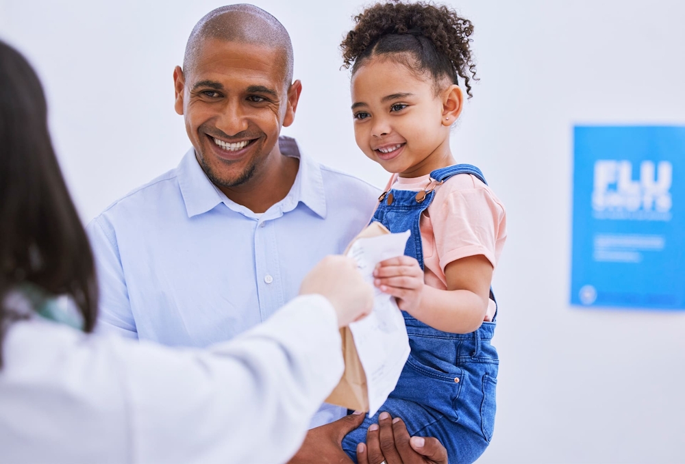 father holding daughter while she grabs medicine from nurse