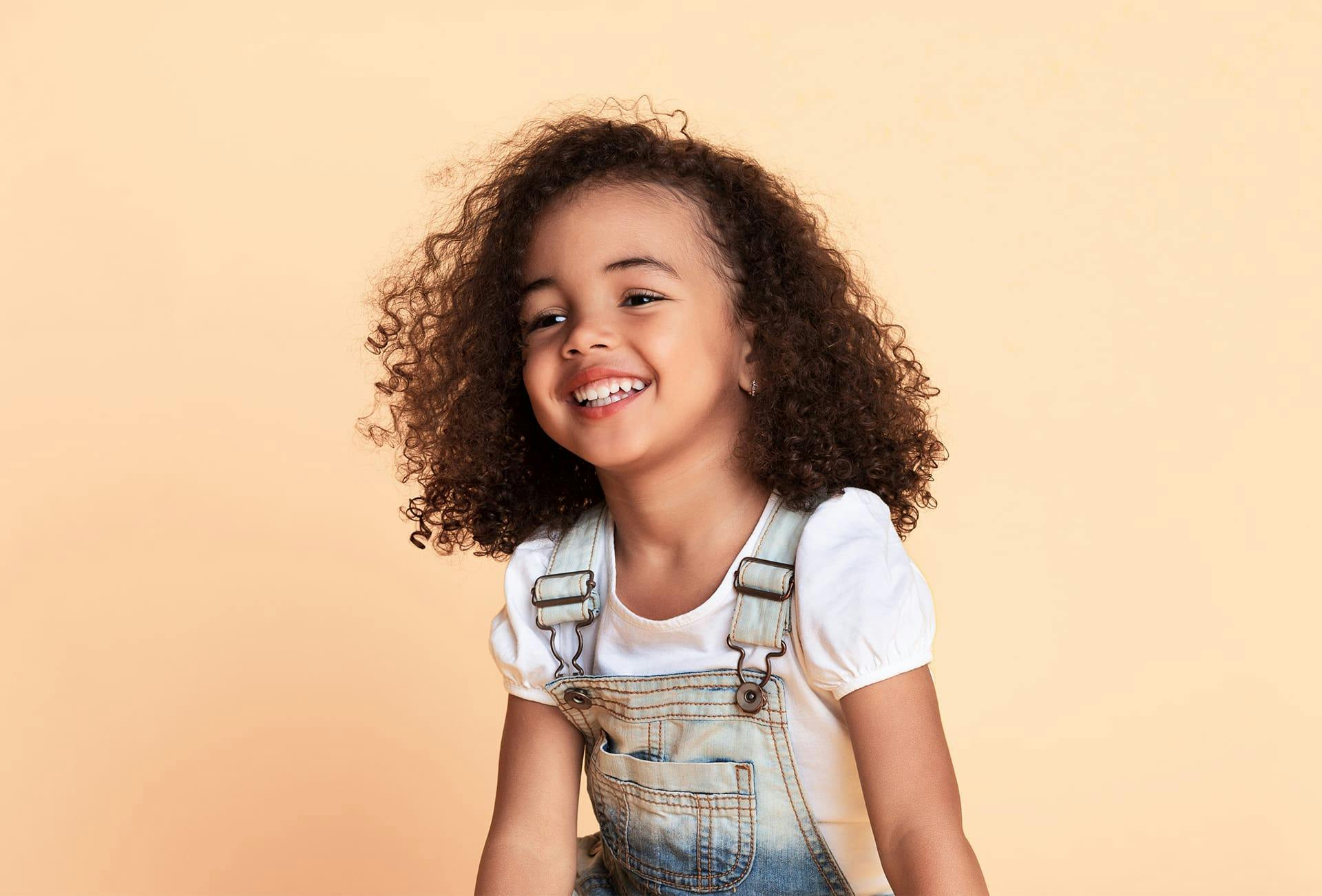 toddler with curly hair in overalls