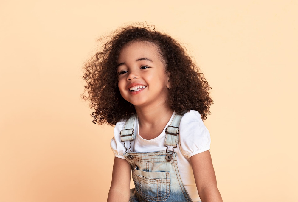 toddler with curly hair in overalls