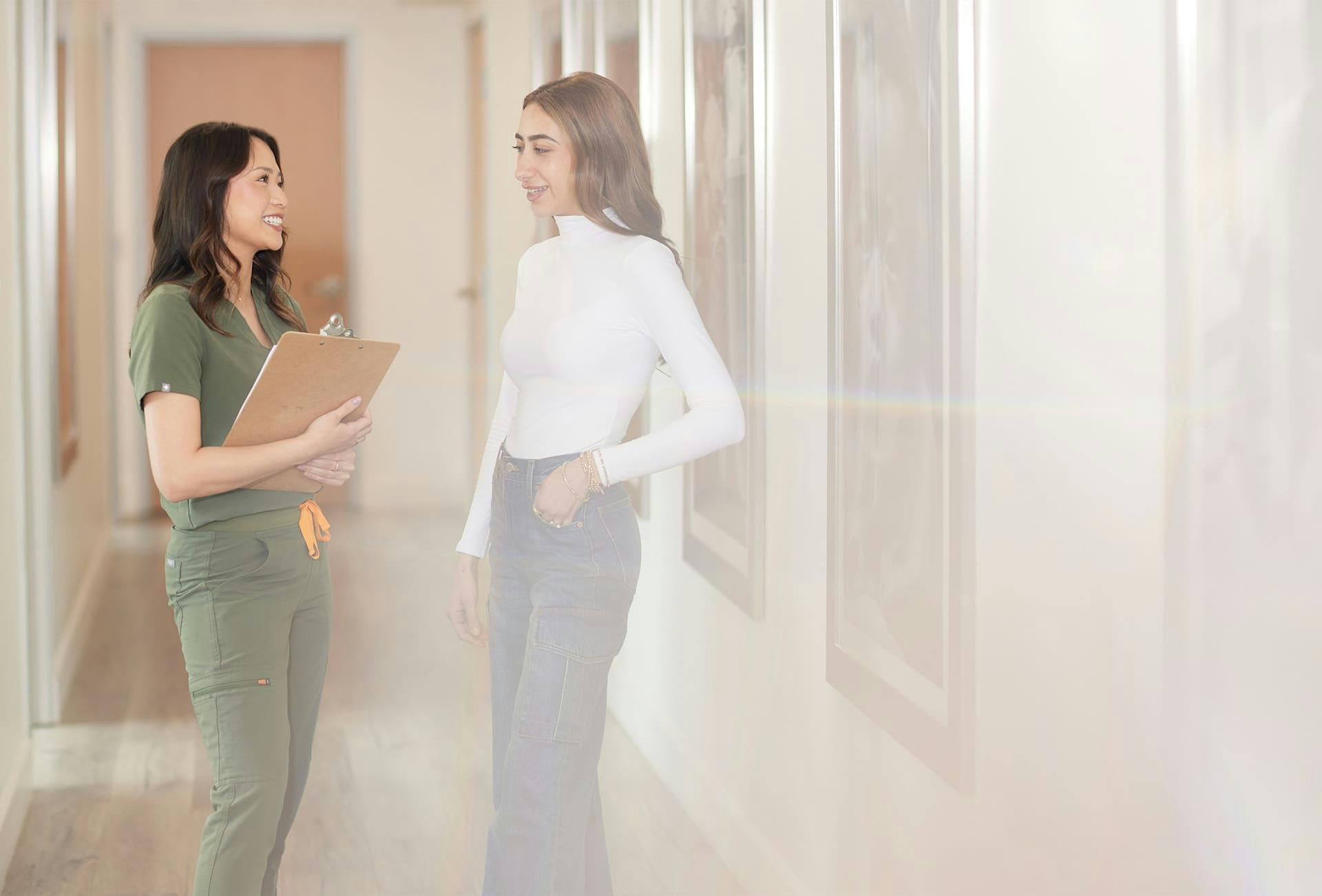 nurse holding clipboard while speaking to patient in hallway