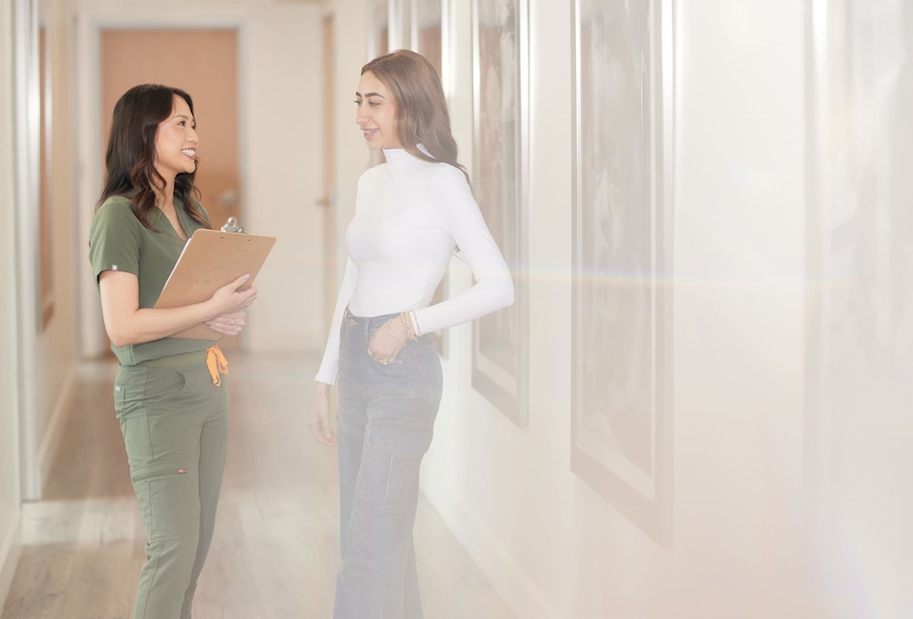 nurse holding clipboard while speaking to patient in hallway