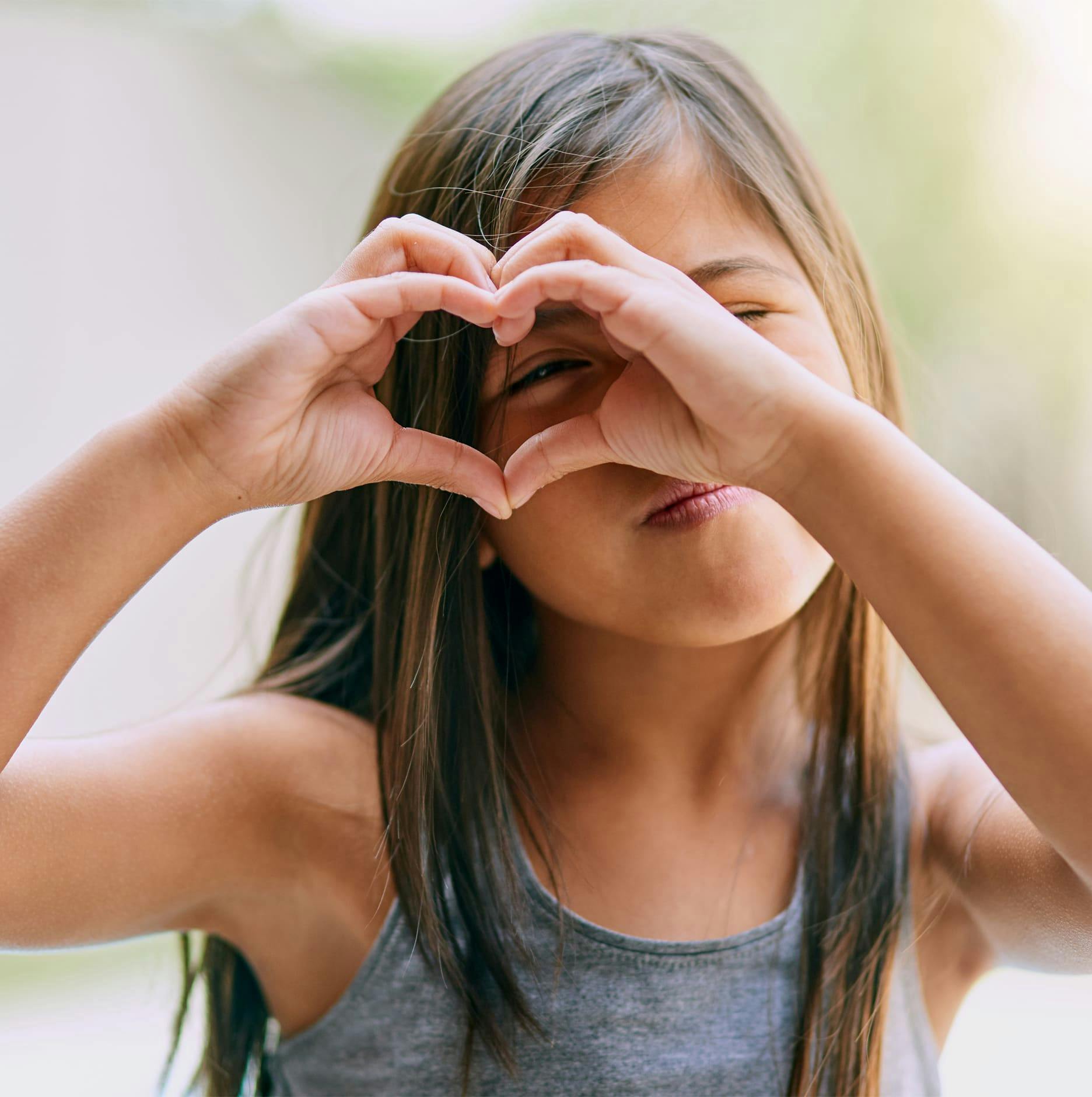 little girl making a heart with hands and looking through it with her eye