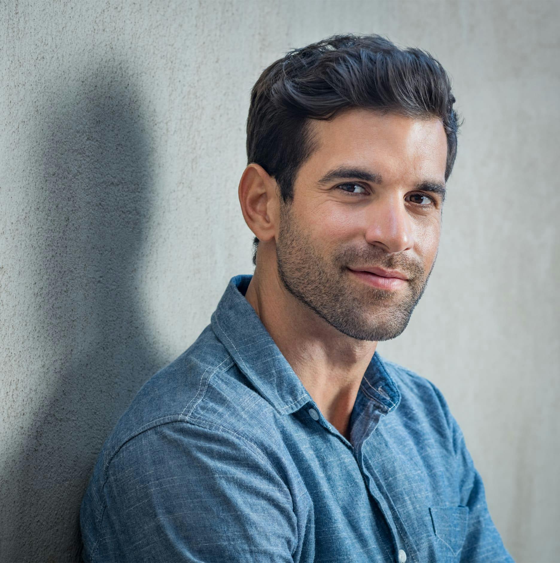man leaning against wall in blue long-sleeve