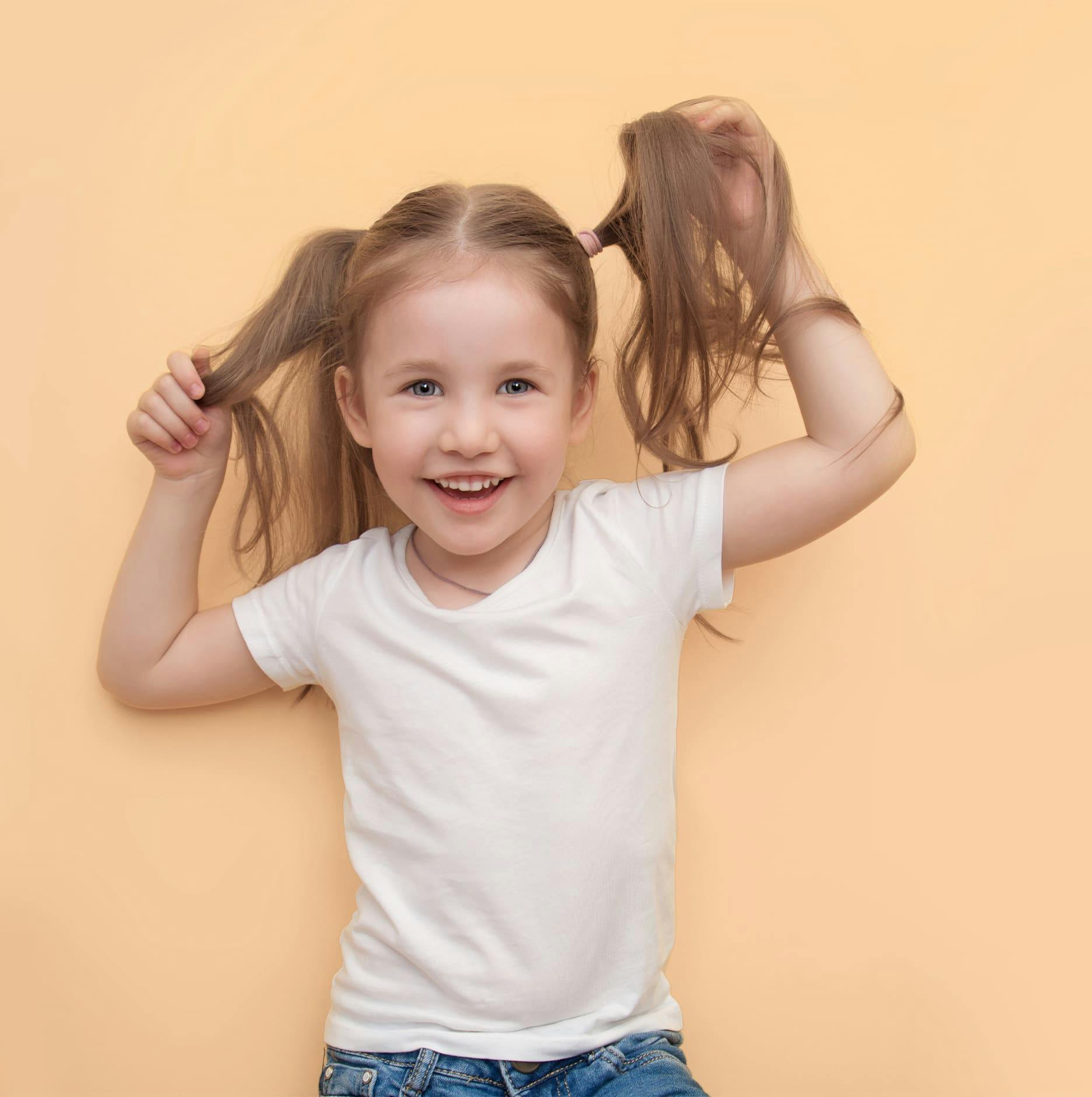 toddler with long blonde pigtails smiling as she touches them