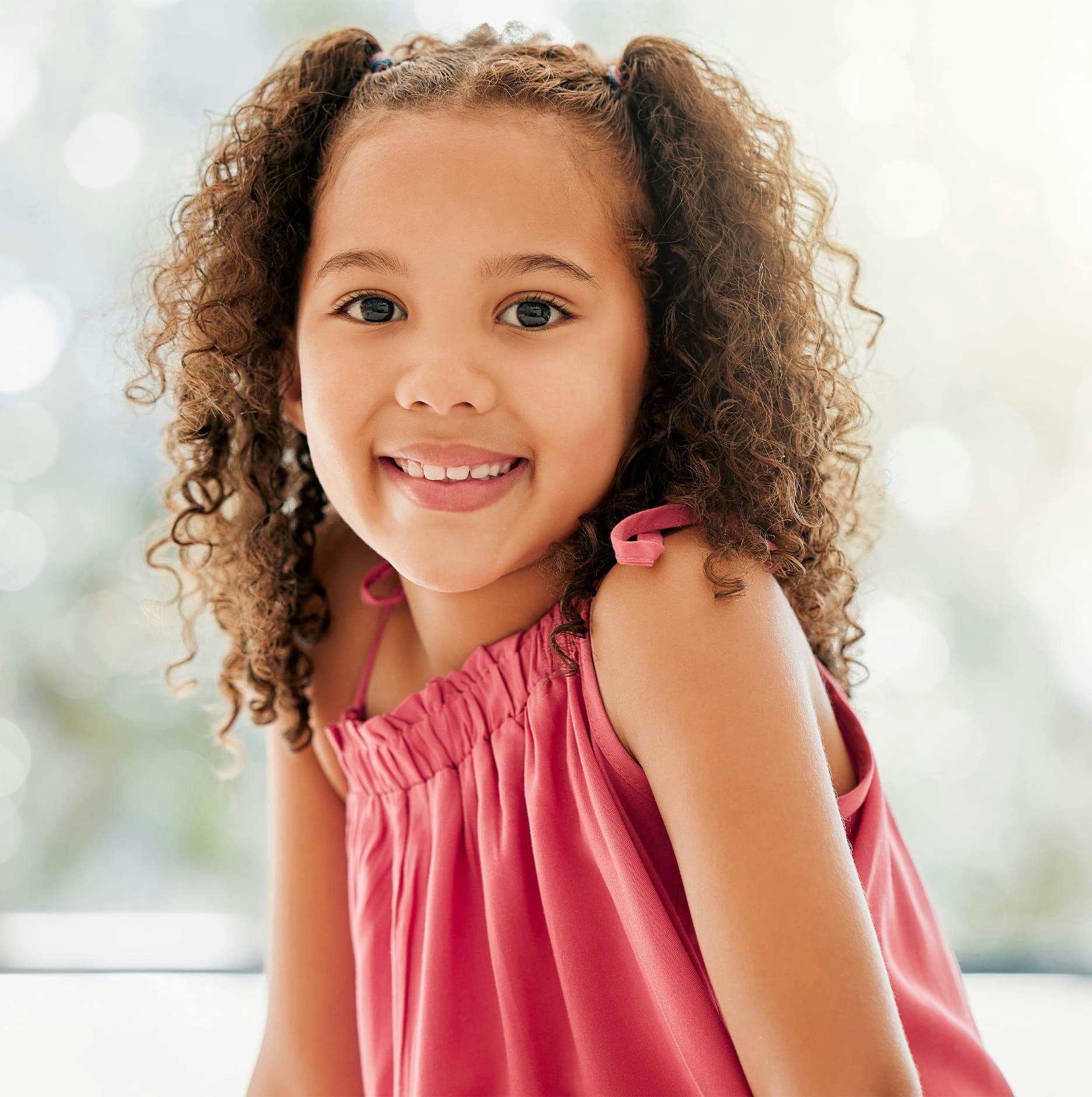 little girl with curly hair and pink dress smiling
