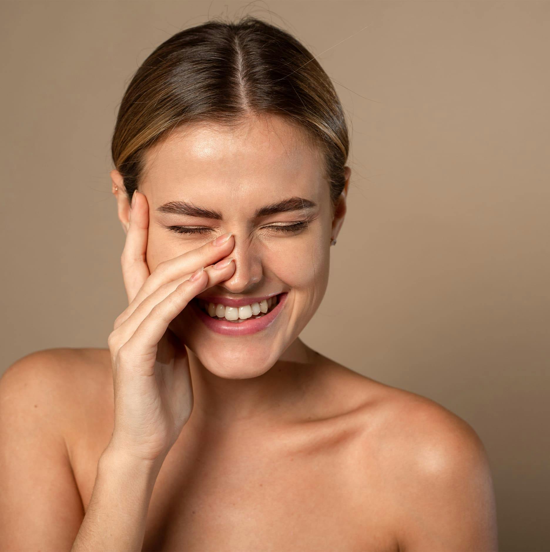 woman with hand around her eyes touching nose and smiling
