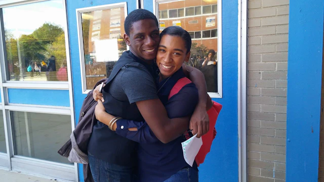 Two teens hugging in front of a building