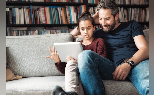 Father and daughter sitting on sofa looking at electronic tablet