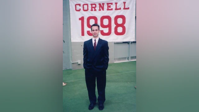 Man in front of Cornell banner