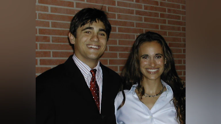 Man and woman smilng in front of brick wall