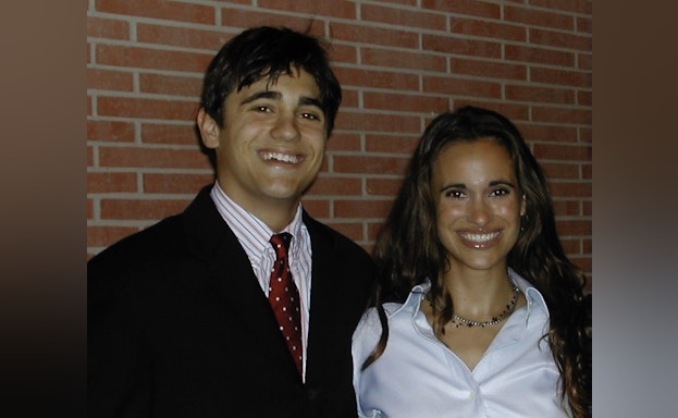 Man and woman smilng in front of brick wall