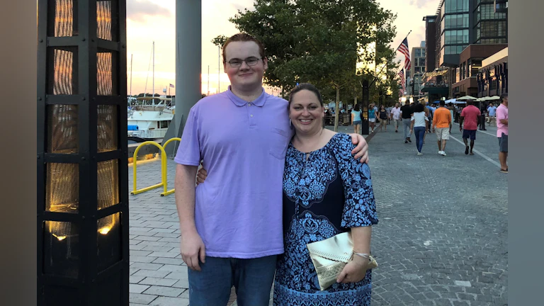 Kathe standing beside her son with her arm around him.