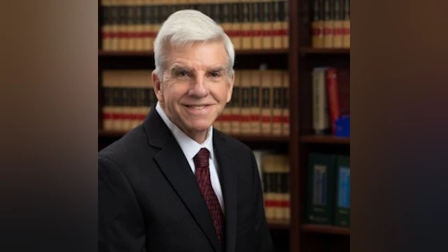 Man in a suit posed in front of a bookshelf