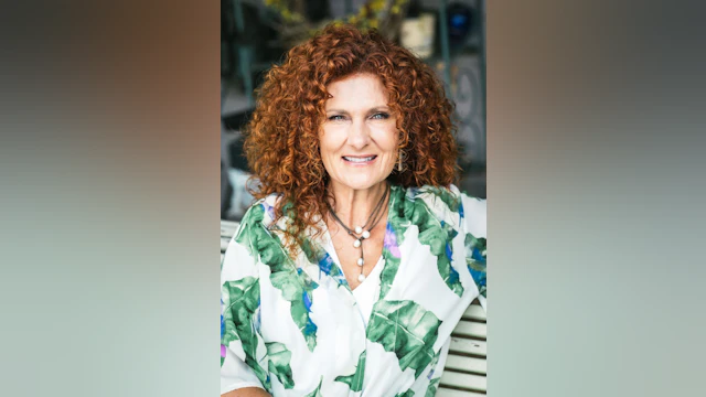 Woman smiling wearing a white shirt with bold green leaves