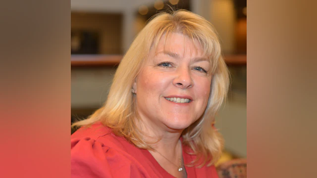 A woman is smiling and wearing a light pink shirt