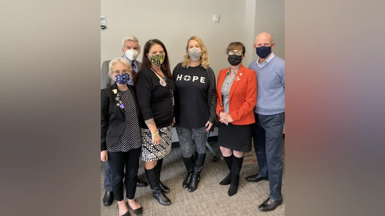 Six people wearing masks stand together for a photograph.