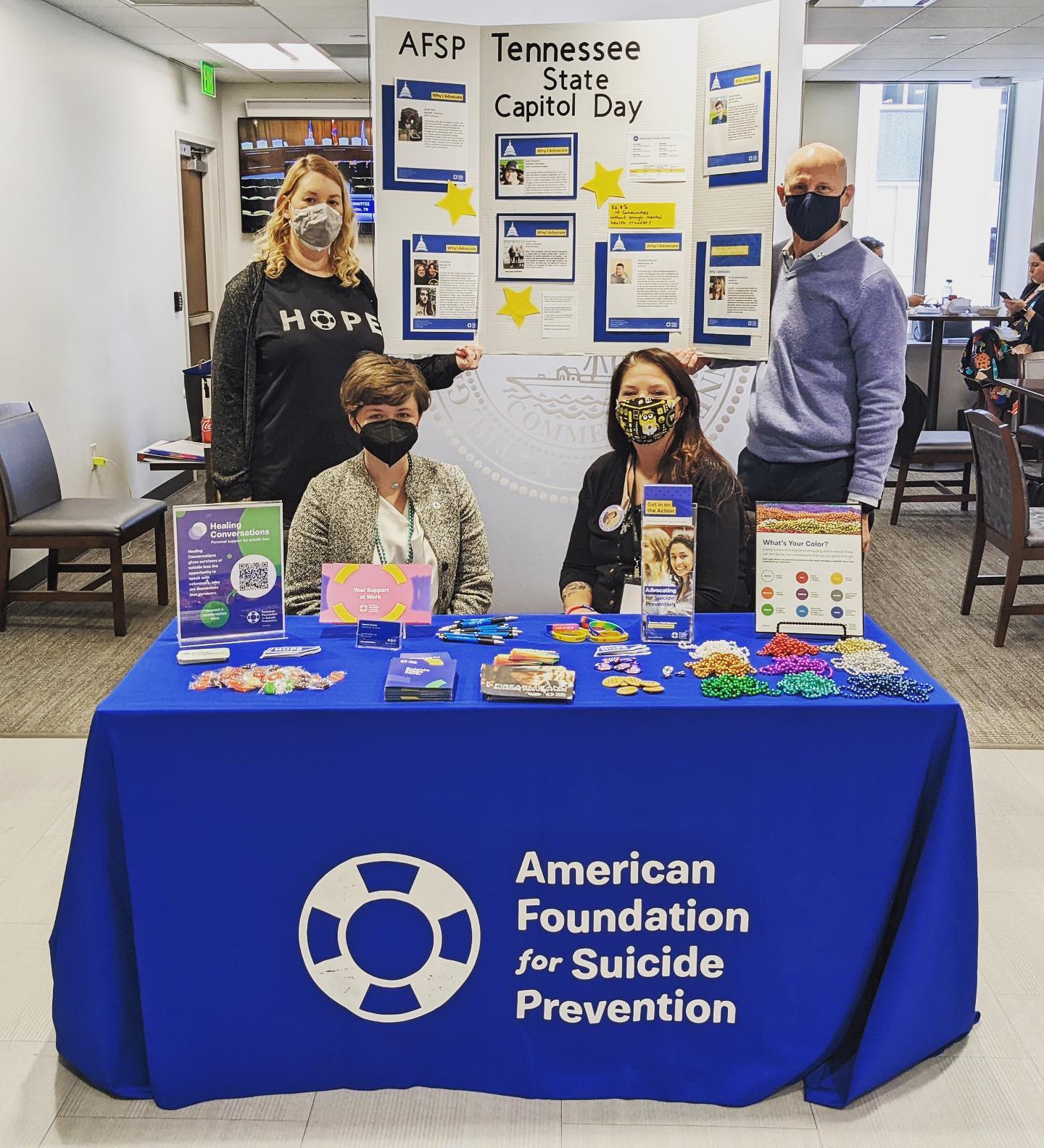 Four people stand around a table with a blue AFSP tablecloth that dispalys various printed materials and AFSP swag.