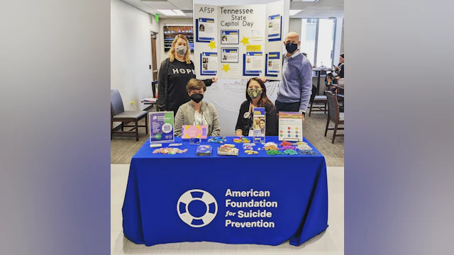 Four people stand around a table with a blue AFSP tablecloth that dispalys various printed materials and AFSP swag.