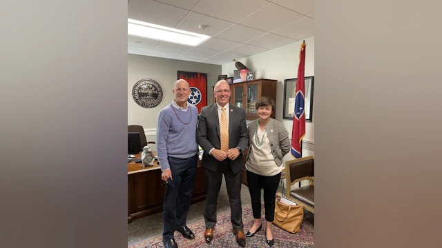 Two men and one women stand and smile in front of a Tennessee state flag.