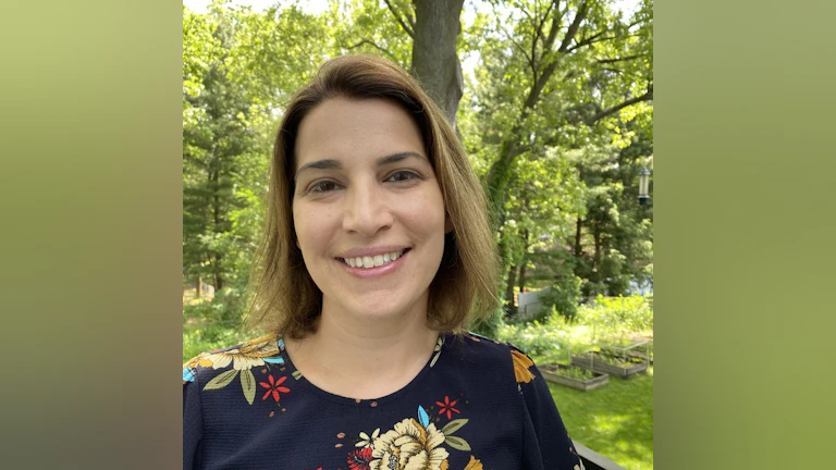 Briana is smiling at the camera and standing in front of trees and the woods