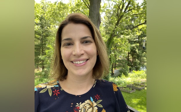 Briana is smiling at the camera and standing in front of trees and the woods