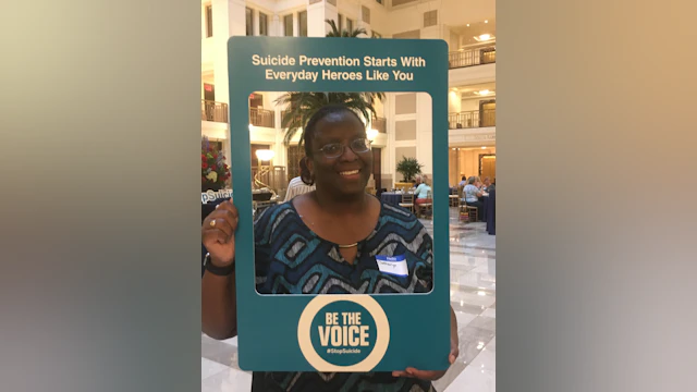 Catharyn Turner posing with a "Be The Voice" photo frame that says, "Suicide Prevention Starts With Everyday Heroes Like You"