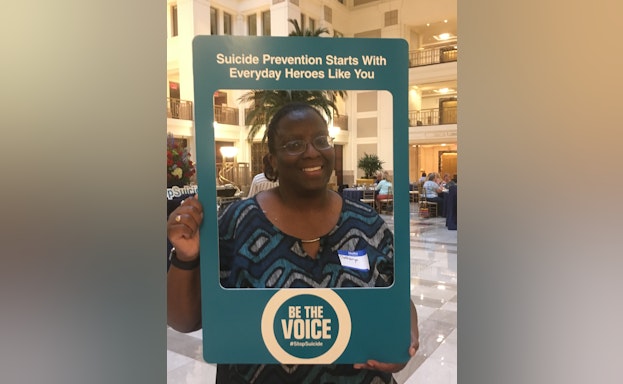 Catharyn Turner posing with a "Be The Voice" photo frame that says, "Suicide Prevention Starts With Everyday Heroes Like You"