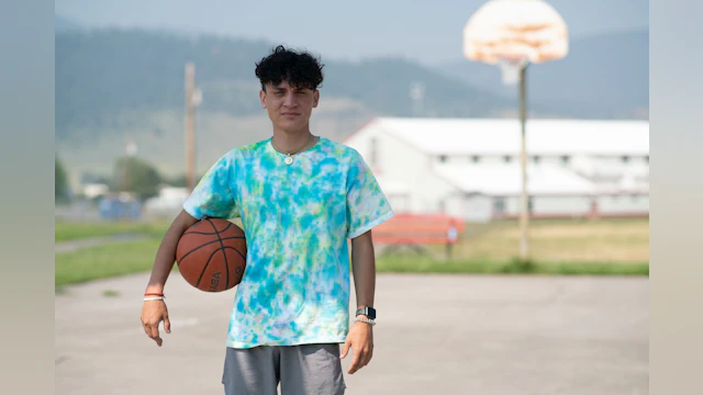 Person stands looking at camera with a basketball under their arm