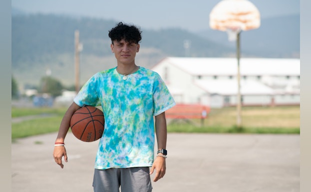 Person stands looking at camera with a basketball under their arm